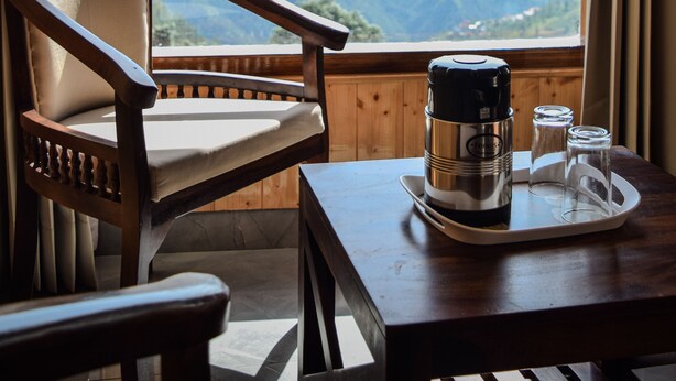 A wooden chair and table with a thermos and salt shakers on a tray, overlooking a mountainous landscape. - Dogri Homes (Shimla)
