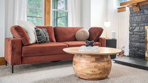 A living room with a red sofa, a round wooden coffee table, and a stone fireplace.
