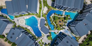 An aerial view of a modern hotel complex with multiple swimming pools, connected by walkways, surrounded by lush greenery and high-rise buildings. - The Title Halo NaiYang by My Home Phuket (Thep Krasattri)