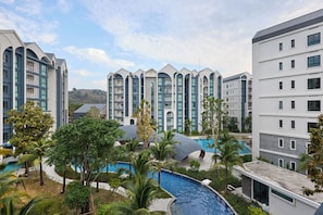 A modern hotel with multiple floors, a swimming pool, and lush greenery.