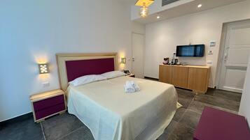 Quarto de hotel com cama, mesas de cabeceira, televisão e minibar.