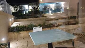 An outdoor seating area with a table and chairs, a staircase, and a view of a lit building in the background.
