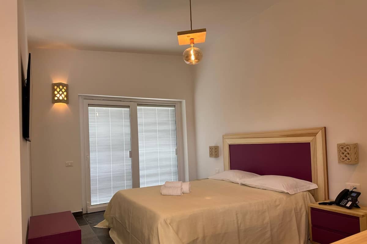 A hotel room with a bed, a nightstand, a telephone, and a wall-mounted light fixture.