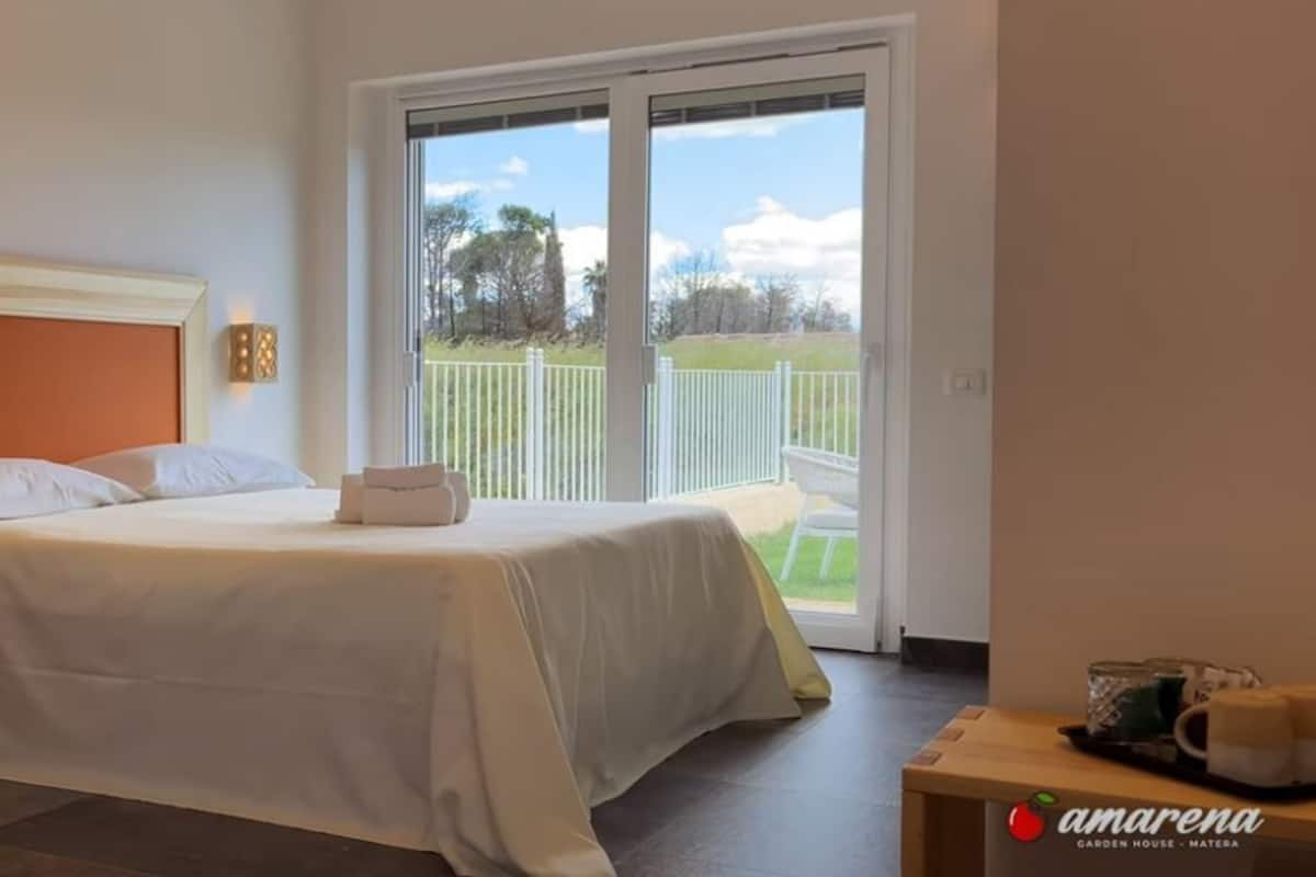 A bedroom with a bed, bedside table with a phone, and a view of a garden through a sliding door.