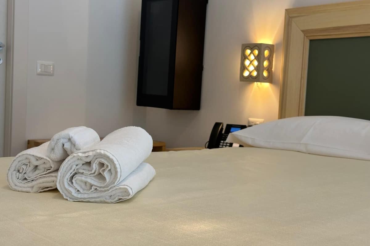 A hotel room with a neatly made bed, a bedside telephone, and a wall-mounted TV.