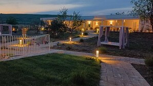 A well-lit outdoor area with a pathway leading to a building, surrounded by a white fence and decorative lighting. - amarena garden house (Matera)