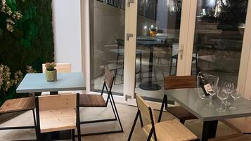 Un'area pranzo all'aperto con una porta vetrata che si apre su un patio, una parete verde con piante e un tavolo con sedie.