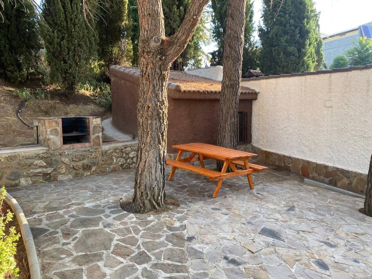 Eine Steinterrasse mit einem Holztisch für ein Picknick, umgeben von Bäumen und einer Steinmauer.