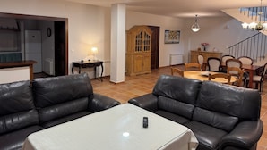 A living room with a sofa, a table, a wooden cabinet, and a dining area with chairs. - San Acacio Mill - Genil Rural House (Huetor De Santillan)