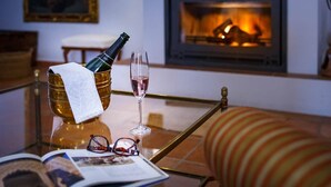 A room with a glass table holding a bottle of champagne, a glass of champagne, and a pair of glasses. There is a fireplace in the background. - San Acacio Mill - Casa Rural Darro (Huetor De Santillan)