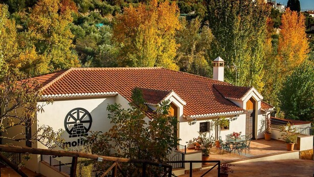 A white building with a red-tiled roof, a chimney, and a sign with a circular logo. - San Acacio Mill - Casa Rural Darro (Huetor De Santillan)