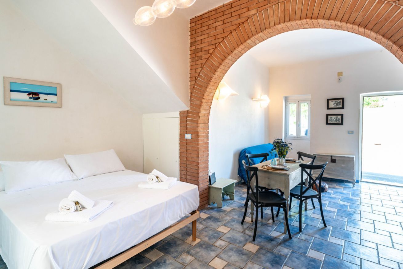 Een hotelkamer met een bed, een zithoek met stoelen en een tafel, en een bakstenen boog.