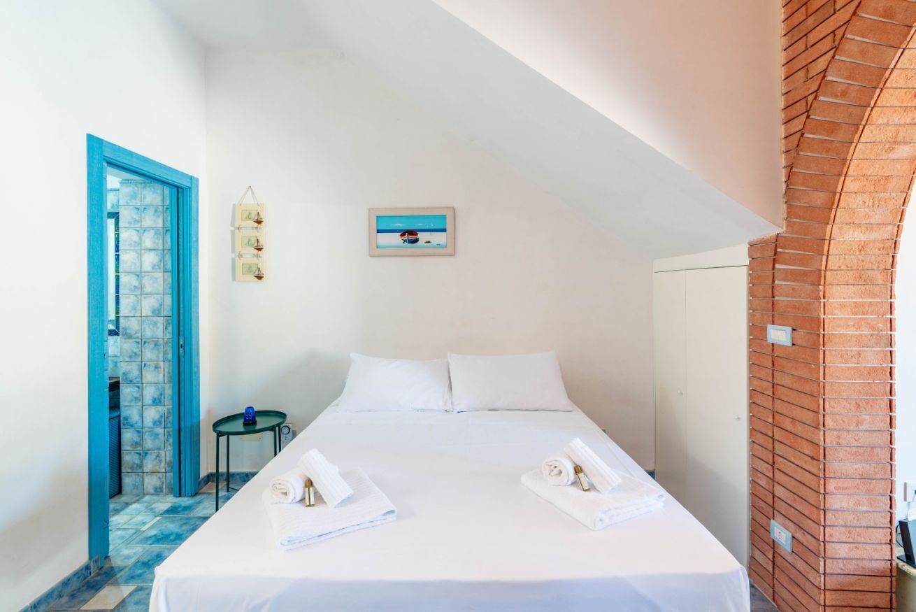 Habitación de hotel con cama, puerta azul, una mesita y un cuadro en la pared.