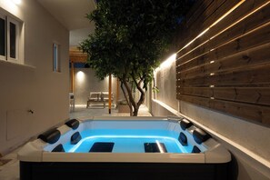 A hot tub in a well-lit outdoor area with a wooden wall and a tree. - Filerimos Nest (Rhodes)