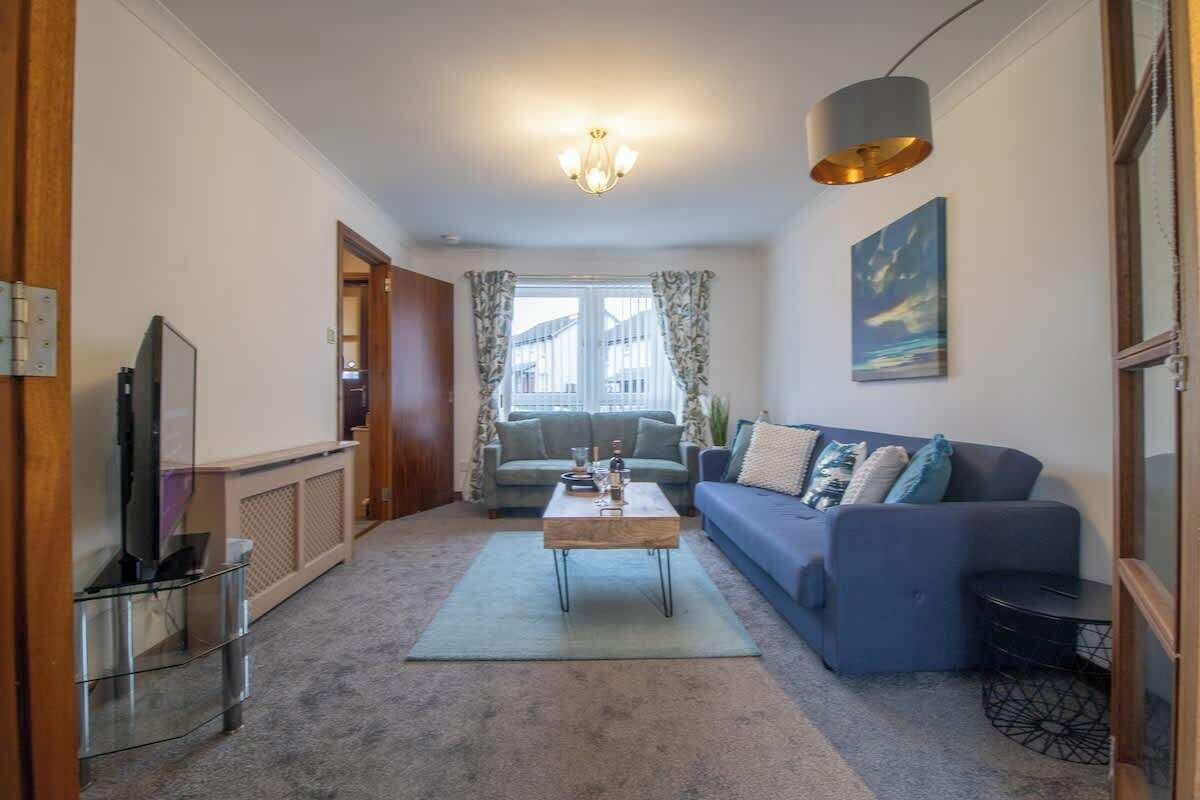 A living room with a sofa, coffee table, TV, and a window with curtains.