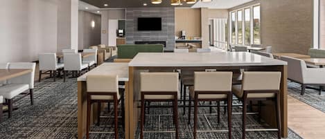 A modern hotel dining area with a large central table, multiple seating options, and a fireplace.