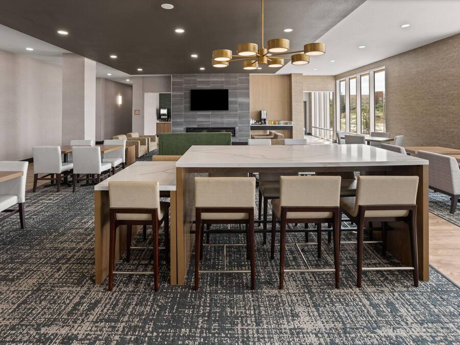 A modern hotel dining area with a large central table, multiple seating options, and a fireplace.