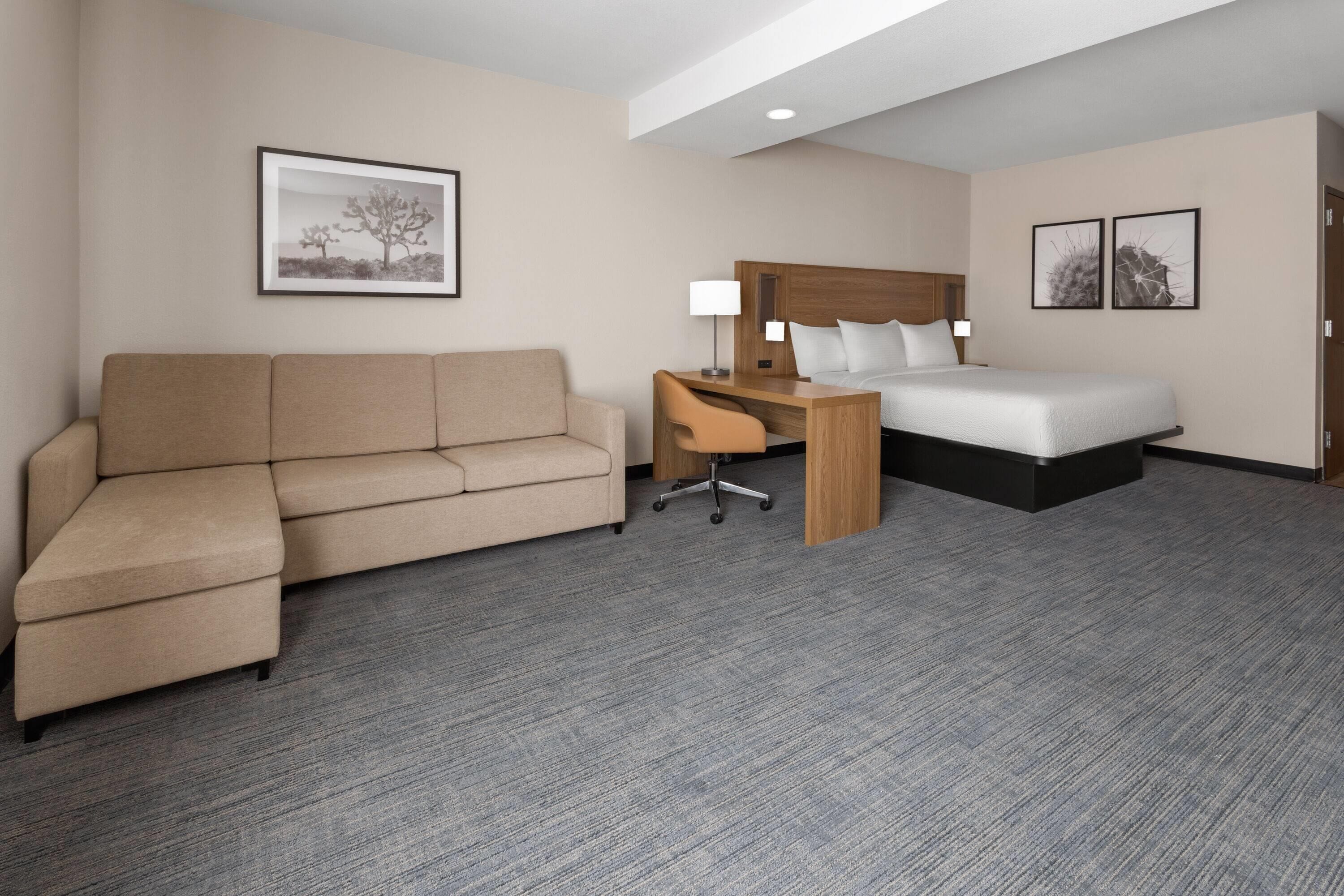 A hotel room with a sofa, a desk, a bed, and two framed pictures on the wall.