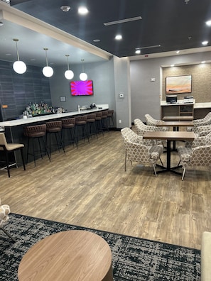 A modern bar area with a counter, stools, and a TV screen. - La Quinta Inn & Suites by Wyndham Phoenix West / Glendale (Phoenix)