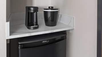 A compact kitchen area with a coffee maker and a trash bin on a white countertop.