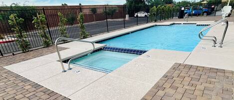 A rectangular swimming pool with a tiled edge, surrounded by a brick patio and metal railings.