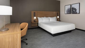 A hotel room with a wooden desk, a single chair, a large bed with a wooden headboard, two bedside lamps, and two framed pictures on the wall.