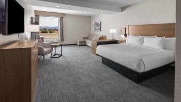 Une chambre d’hôtel avec un grand lit, un bureau avec une chaise, un canapé, une télévision et une fenêtre donnant sur les montagnes.