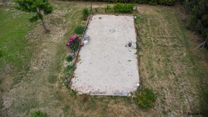 Une vue aérienne d’une zone extérieure rectangulaire, recouverte de sable, et entourée d’herbe et de petites plantes.