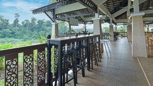 An outdoor bar area with high stools, a view of the forest, and a covered seating area with a patterned ceiling. - Hotel O Asiacamp Resort National Park Kuala Tahan (Kuala Tahan)