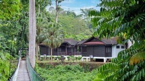 A wooden suspension bridge over a lush green area with traditional-style buildings in the background. - Hotel O Asiacamp Resort National Park Kuala Tahan (Kuala Tahan)