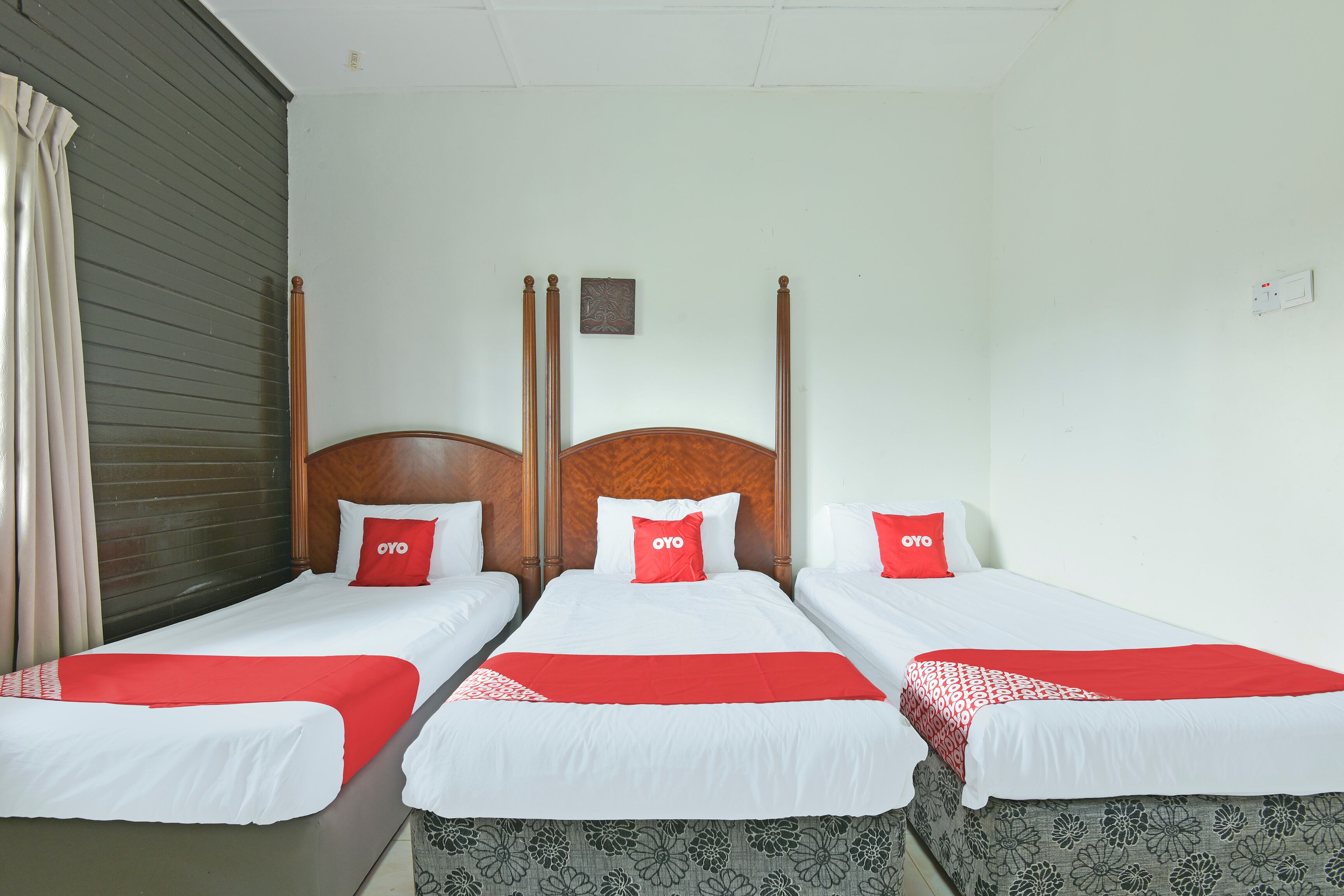Une chambre d’hôtel avec trois lits simples, chacun doté d’une tête de lit en bois, de draps blancs et d’oreillers rouges.
