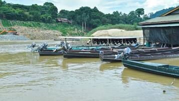 A river with several boats docked, a construction site in the background, and a building with a thatched roof.
