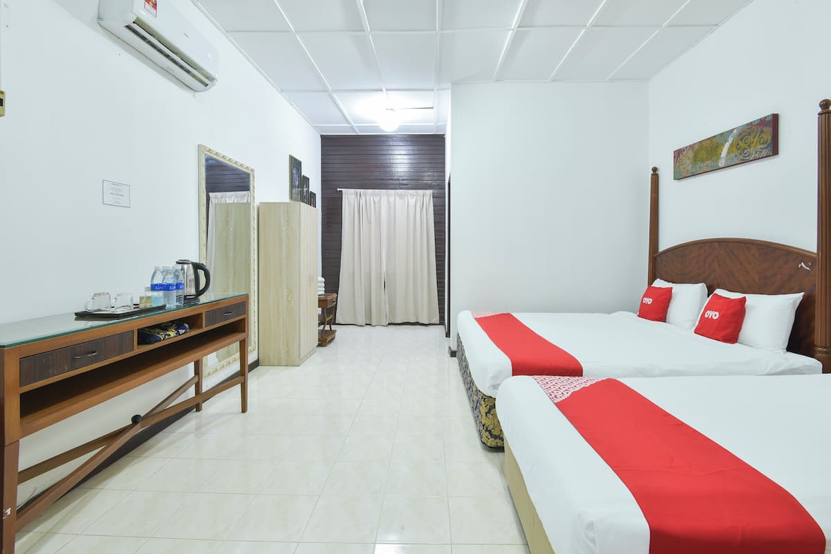 Quarto de hotel com duas camas, uma escrivaninha de madeira, um guarda-roupa e um banheiro visível por uma cortina.