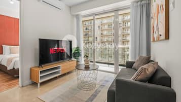 A modern living room with a flat-screen TV, a sofa, a coffee table, and a large window with a view of a residential building.