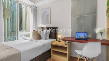 A hotel room with a bed, a desk with a laptop, a chair, and a window with curtains.