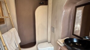 A compact bathroom with a white toilet, a black sink, a shower, and a small mirror. - Villa Pasithea, Finikia, Oia, Santorini (Oia)