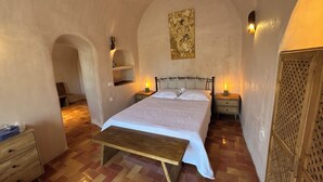 A bedroom with a bed, bedside tables, a bench, and a wall-mounted shelf. - Villa Pasithea, Finikia, Oia, Santorini (Oia)