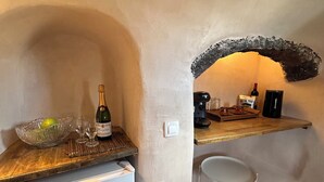 A compact kitchen with a refrigerator, a wooden counter, a bowl with fruit, wine glasses, and a bottle of wine. - Villa Pasithea, Finikia, Oia, Santorini (Oia)