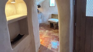 A narrow hallway with a tiled floor, a wooden bench, and a small window with a lattice design. - Villa Pasithea, Finikia, Oia, Santorini (Oia)