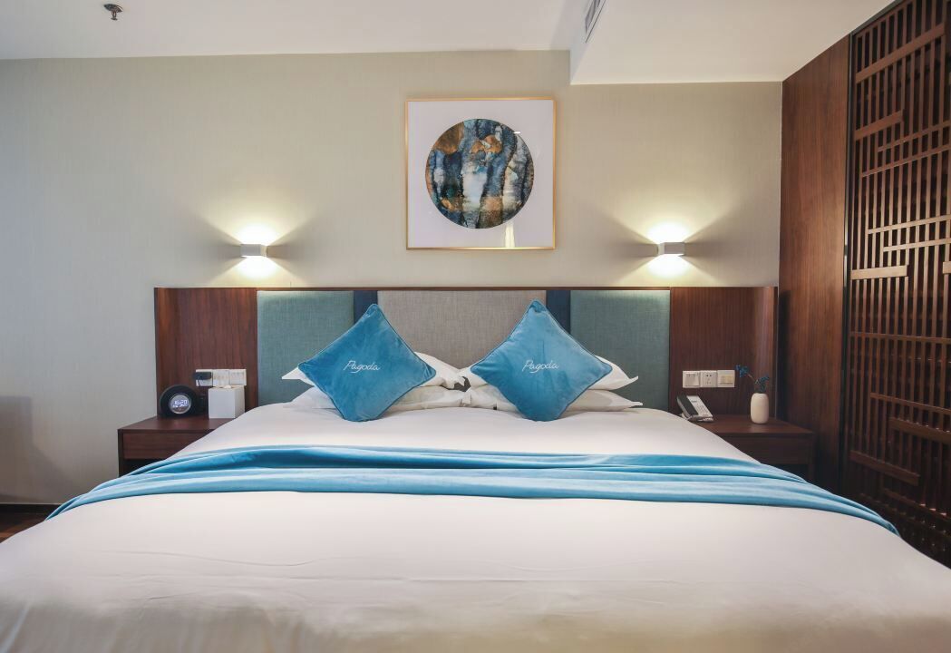 Una habitación de hotel con cama, dos mesitas de noche, una obra de arte colgada en la pared y un separador decorativo.