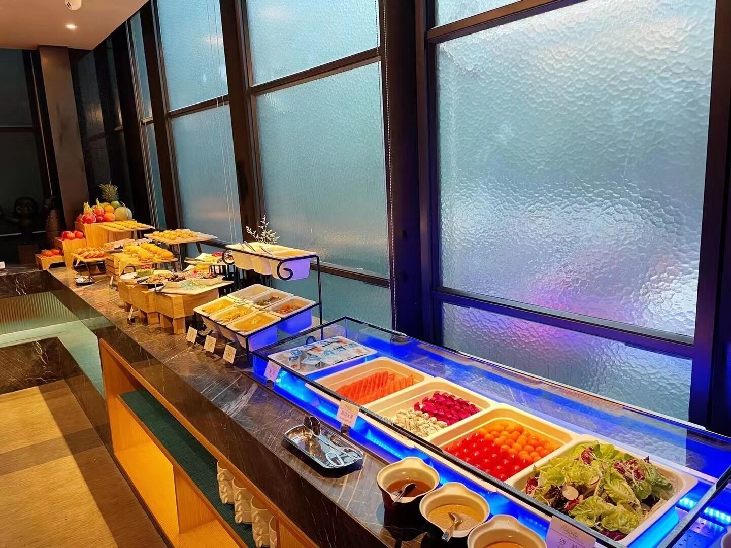 A buffet with various food items and drinks, arranged on a counter with a glass display case.