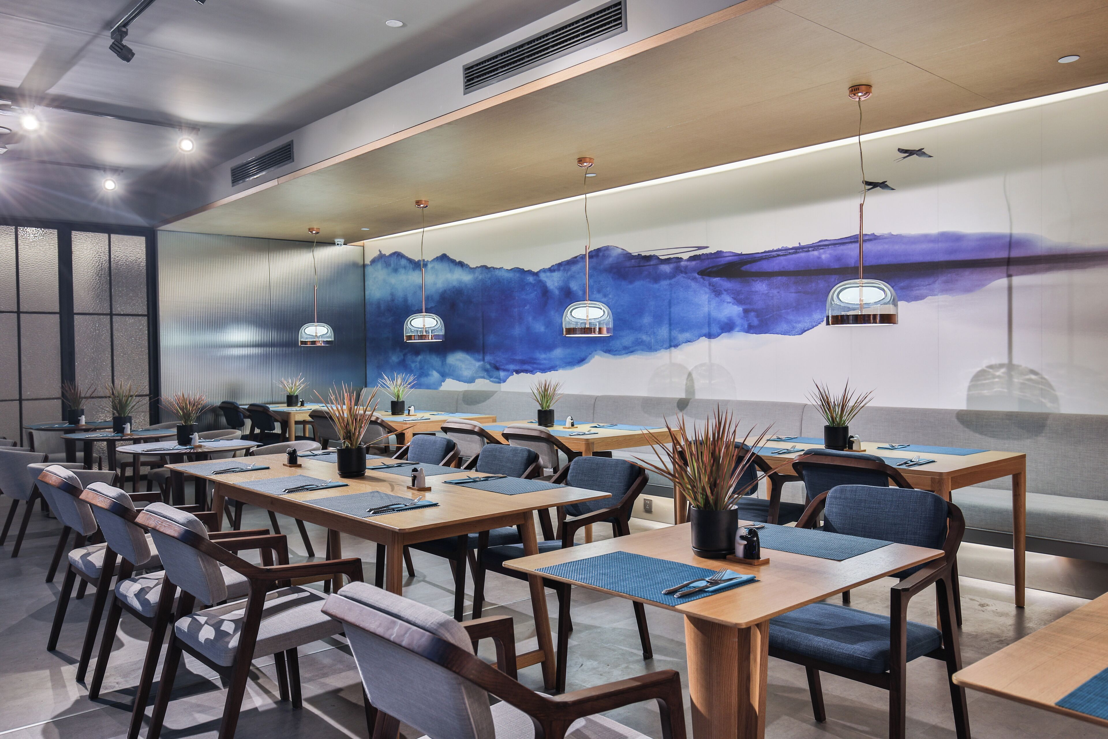 A modern conference room with wooden tables and chairs, a large mural on the wall, and pendant lighting.