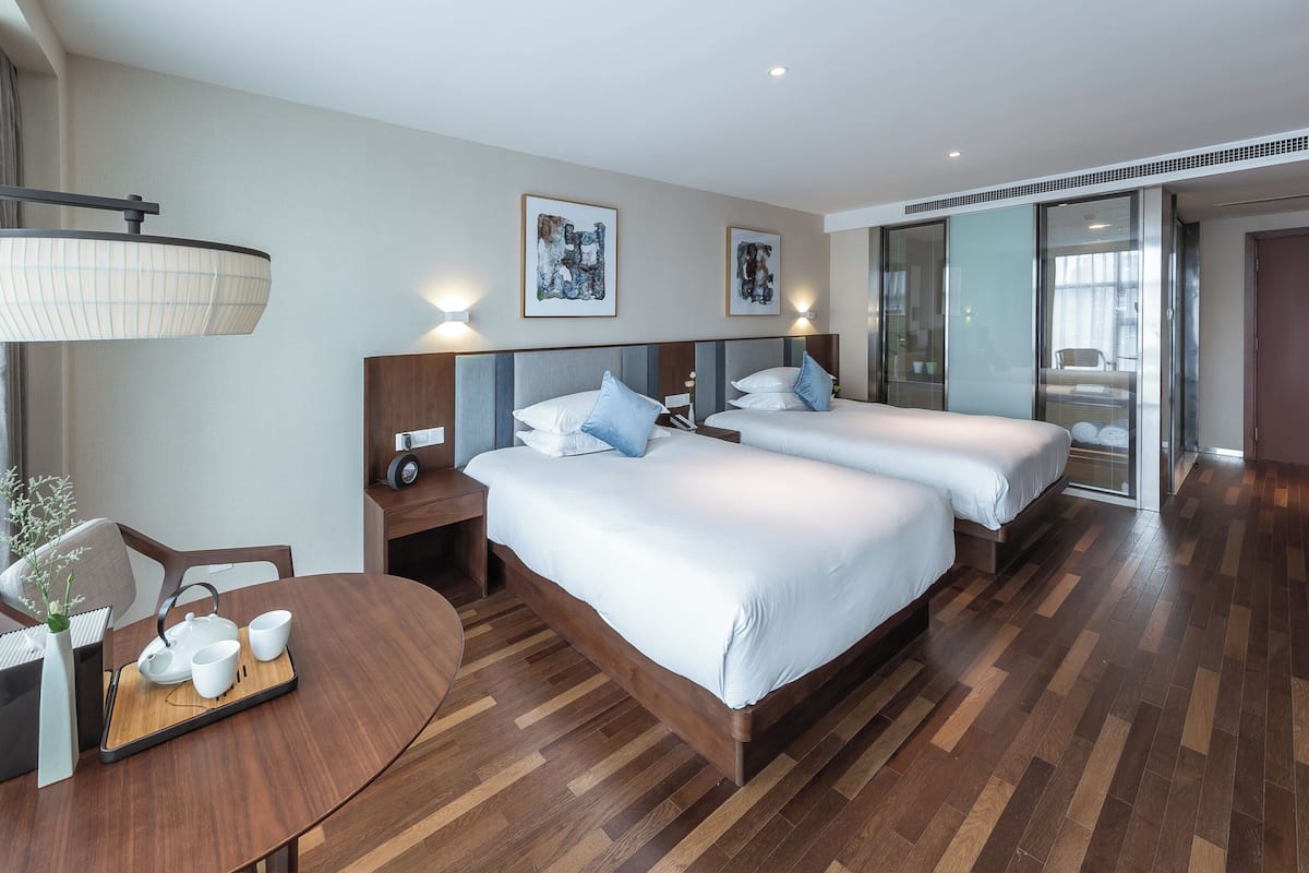 Ein Hotelzimmer mit zwei Betten, einem Holztisch mit einer Kaffeetasse und einer Lampe, sowie Bildern an den Wänden.