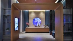 Un'area reception moderna con una scrivania centrale, un grande display digitale circolare e un angolo salotto con poltrone.