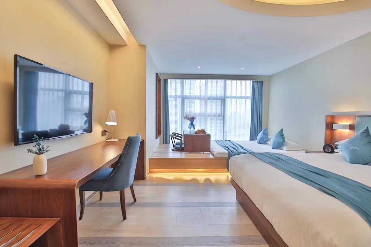 Ein modernes Hotelzimmer mit Bett, Schreibtisch, Stuhl, Fernseher und großen Fenstern.