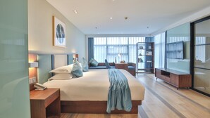 Una camera d'hotel moderna con un letto grande, comodini, una TV, una libreria e un'ampia finestra che offre luce naturale.
