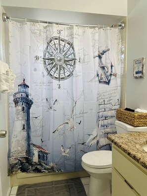 Une salle de bain avec un rideau de douche à motifs nautiques, une illustration représentant un phare et un panneau indiquant « Veuillez » accroché au mur.