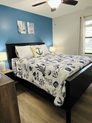 Une chambre à coucher avec un lit, une table de chevet, un ventilateur de plafond et une fenêtre avec des rideaux.