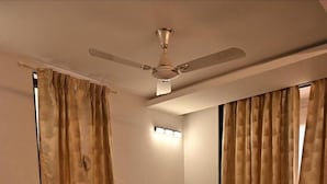 A neatly made bed with a headboard, a nightstand with a lamp, and a ceiling fan. - Shreejee Villa (Mahabaleshwar)