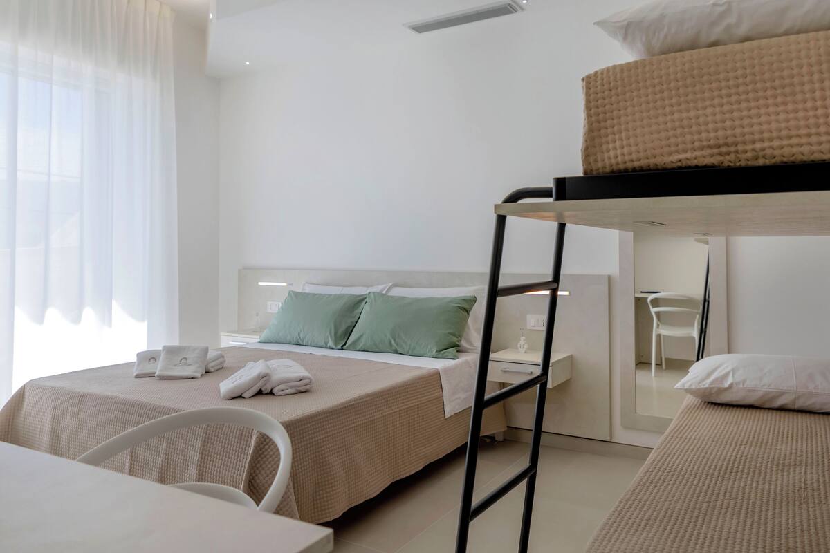 A hotel room with a bunk bed, a desk, a chair, and a bedside table.